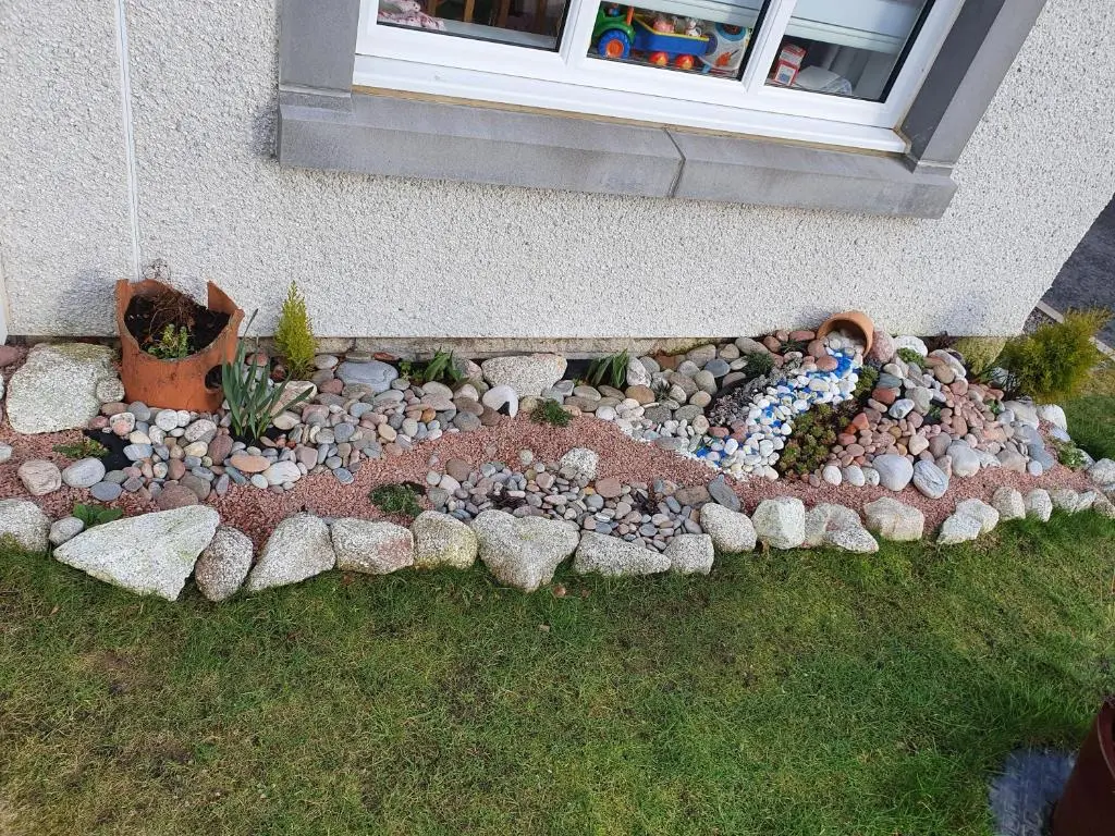a garden with rocks and a child laying on the grass at Kellys in Inverness