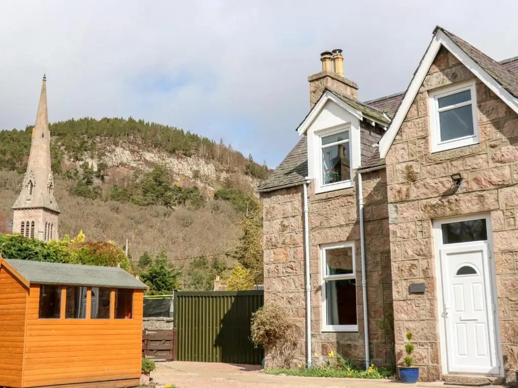 an old stone house with a church in the background at Gairnlea Cottage in Ballater
