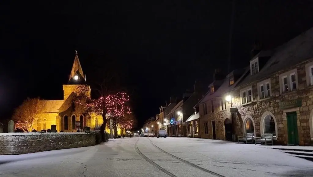 a snowy street at night with a church at Balloan Cottage in Dornoch