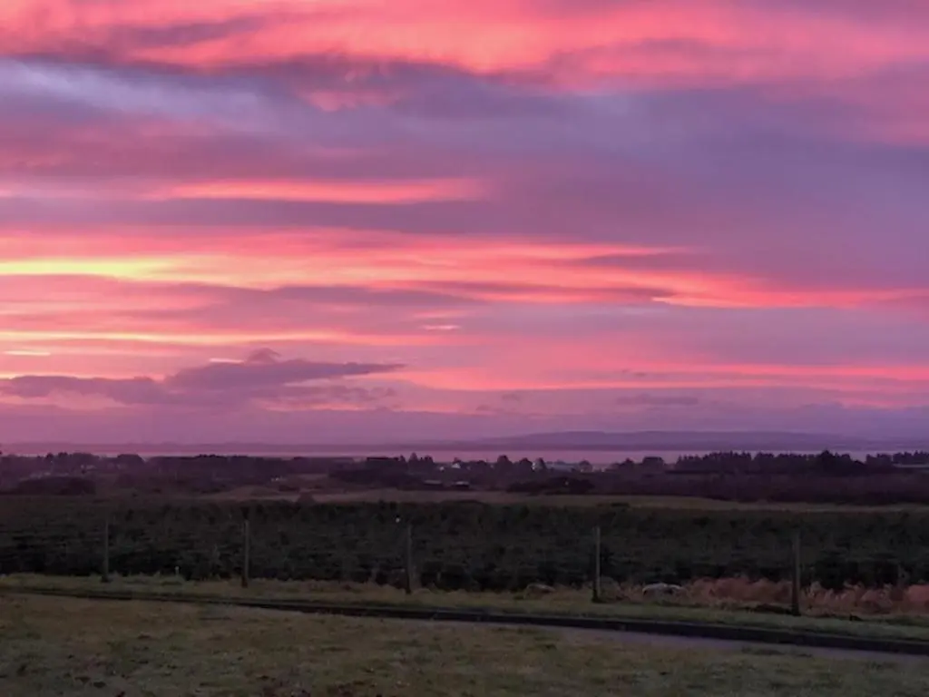 a sunset over a field with a fence at Balloan Cottage in Dornoch