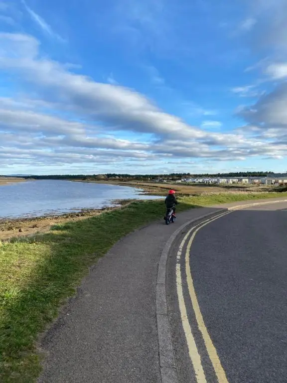 a person riding a motorcycle on a road near the water at Beachfront Lodge, Lossiemouth Bay in Lossiemouth
