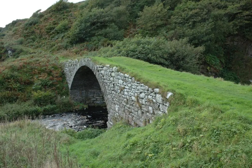 an old stone bridge over a river in a field at Craiglea Lodge & Barn in Latheron