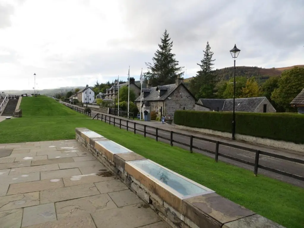 a street in a town with a fence and grass at Glenwood Apartment at The Highland Club in Fort Augustus
