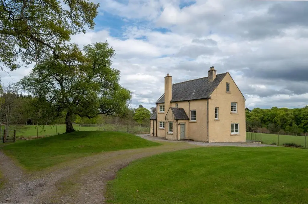 an old house on a grassy field next to a dirt road at Braemoray in Evanton