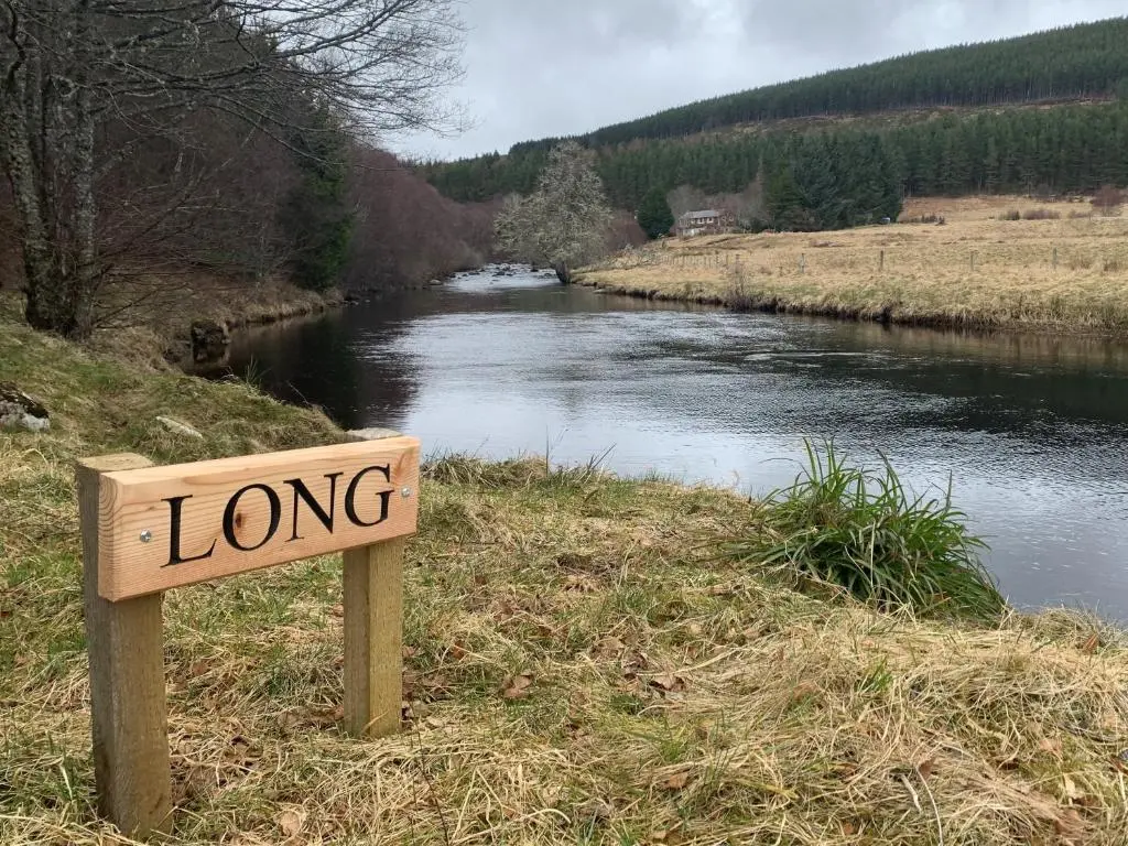 a sign that reads long next to a river at Strone in Boath