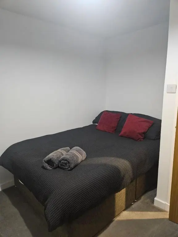 a bed with a black comforter and red pillows at No 14, 3 BED all with SMART TV's, Fully Fitted Kitchen, Ample PARKING, Ideal for TRADES, BUSINESS wanting comfort and a quality service REDUCTIONS FOR LONGER STAYS Langley Cottages and Apartments, in Wick