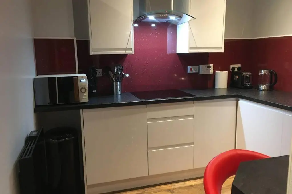 a kitchen with white cabinets and a red wall at Modern 1 Bedroom Apartment central Inverness city in Inverness