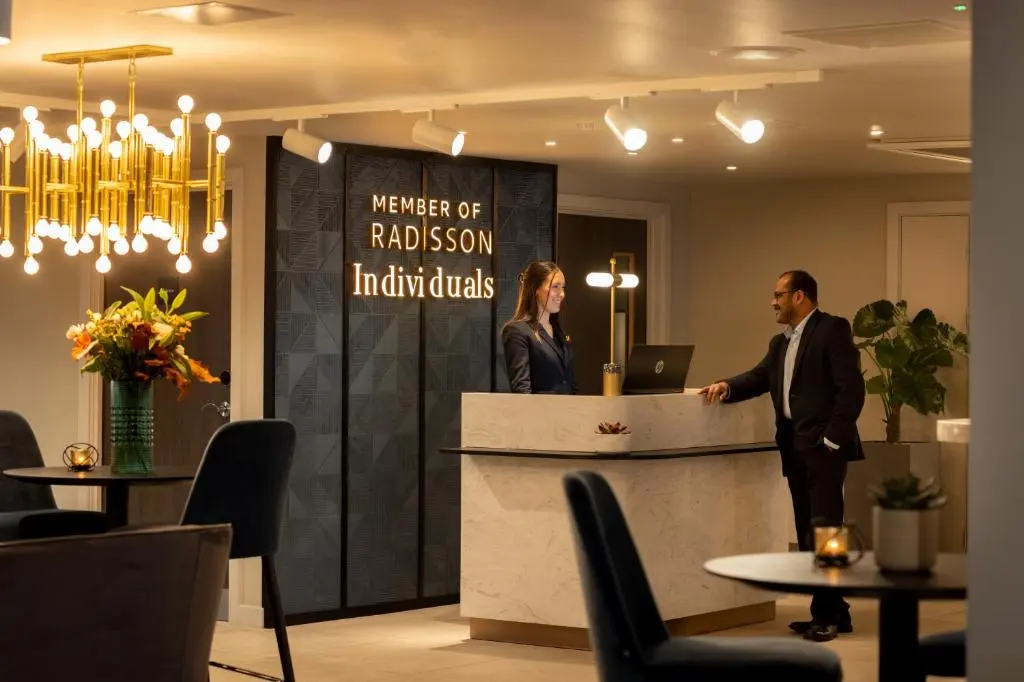 a man and a woman standing at a reception counter at River Ness Hotel, a member of Radisson Individuals in Inverness
