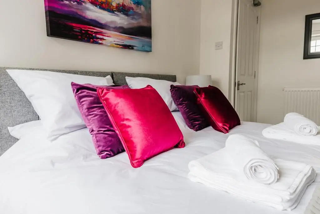 a white bed with red and purple pillows on it at Seaforth House Apartment in Elgin