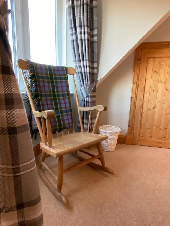 a wooden rocking chair sitting next to a window at Islas Cottage, a home in the Heart of Speyside in Dufftown
