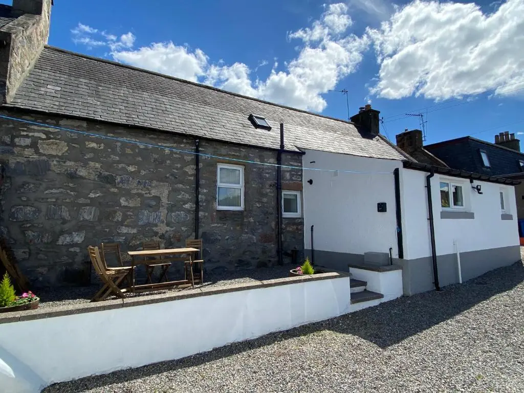 a stone house with a table and a bench outside at Islas Cottage, a home in the Heart of Speyside in Dufftown