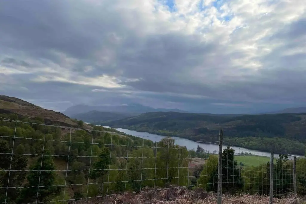 a fence on a hill with a river in the background at Coorie Doon Cabin! Great Scottish Welcome in Fort Augustus