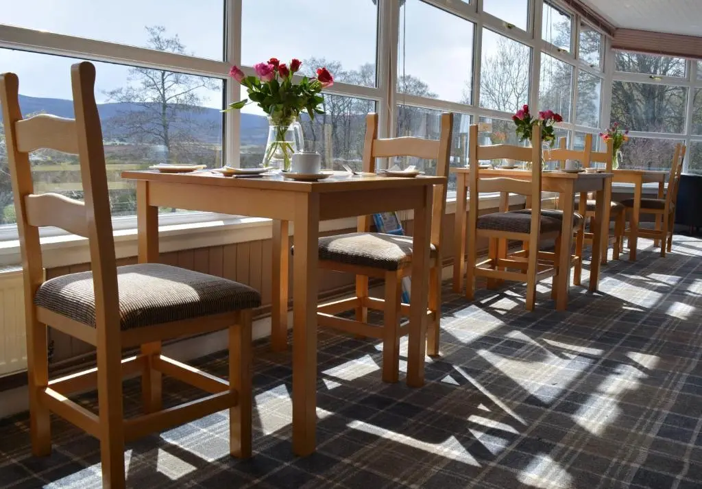 a table and chairs in a room with windows at Feughside in Strachan