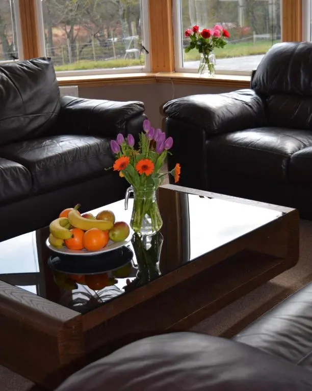 a coffee table with a vase of flowers and fruit on it at Feughside in Strachan