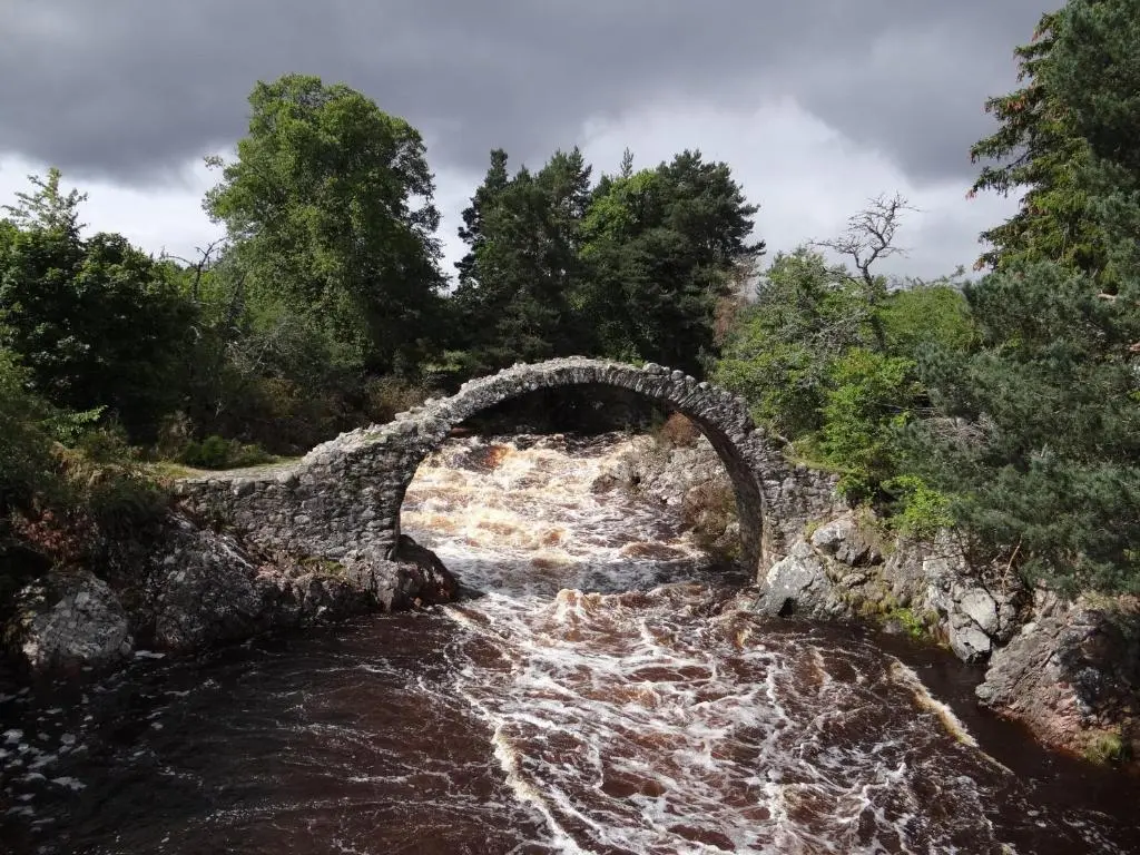 an old stone bridge over a river with water at The Cottage Bogroy in Carrbridge