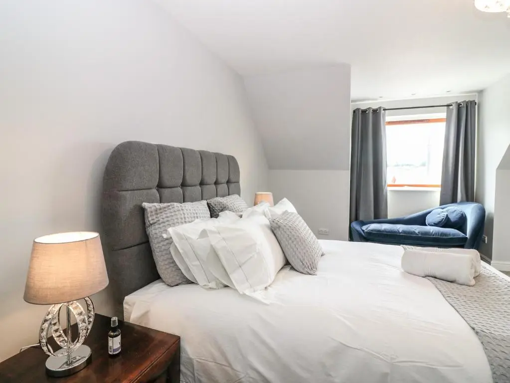 a bedroom with a large white bed and a blue chair at Tombeck in Tomintoul