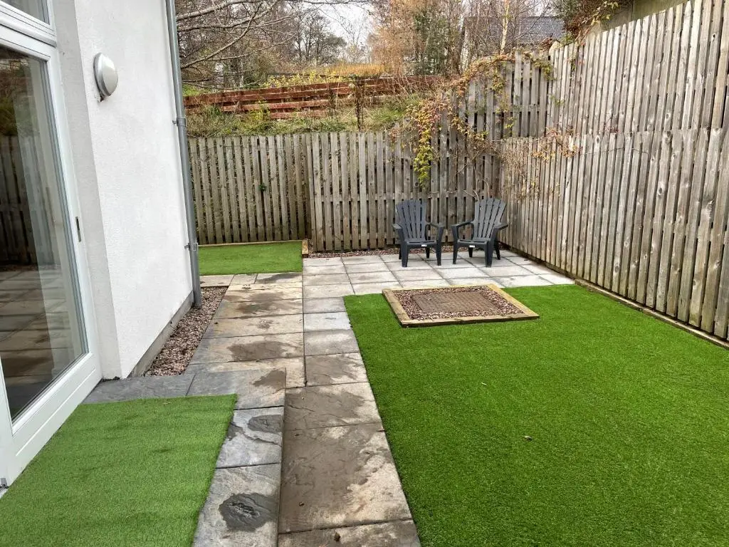 a patio with a bench and grass in front of a fence at Woodside retreat holiday home in Aviemore in Aviemore