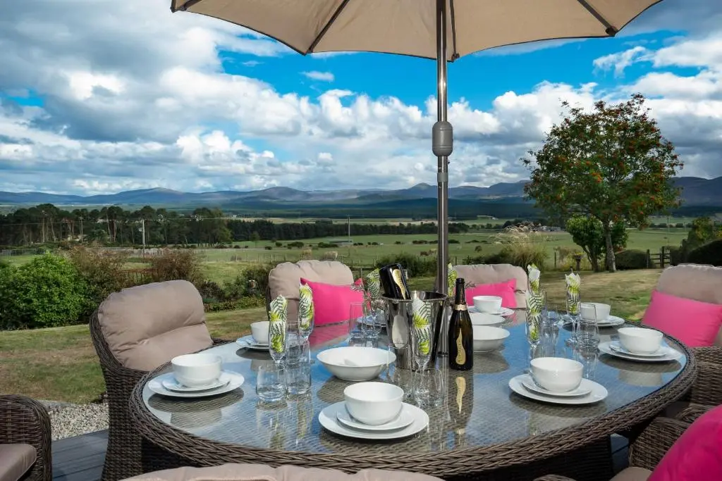 a table with chairs and an umbrella on a patio at The Eagle's Nest - large house with hot tub and sauna in Boat of Garten