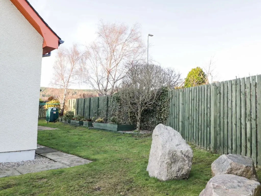 a yard with a fence and two large rocks at 3 Croftside in Aviemore