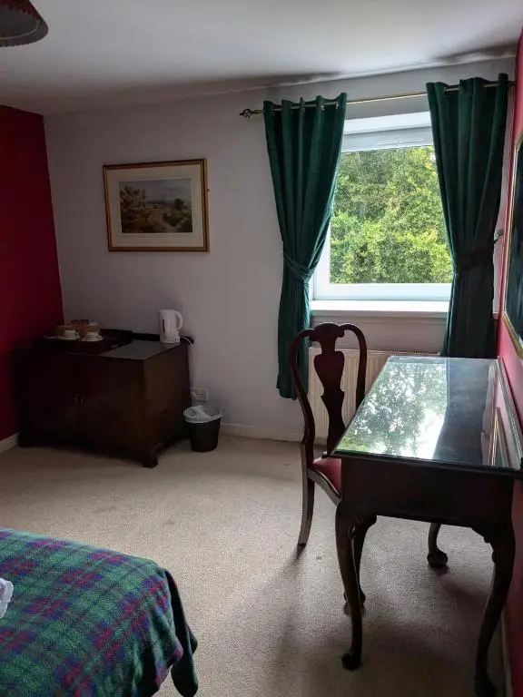 a bedroom with a bed and a table and a window at Bennachie Lodge Hotel in Kemnay in Inverurie