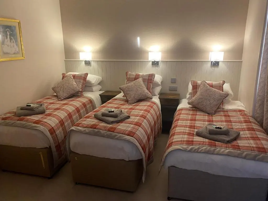 a hotel room with three beds with towels on them at Adrian's Guest House in Inverness