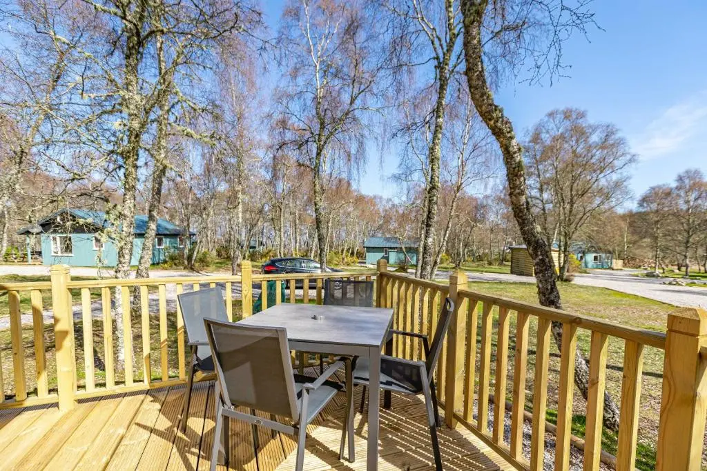 a table and chairs on a wooden deck at Thistle Lodge 21 with Hot Tub in Belladrum
