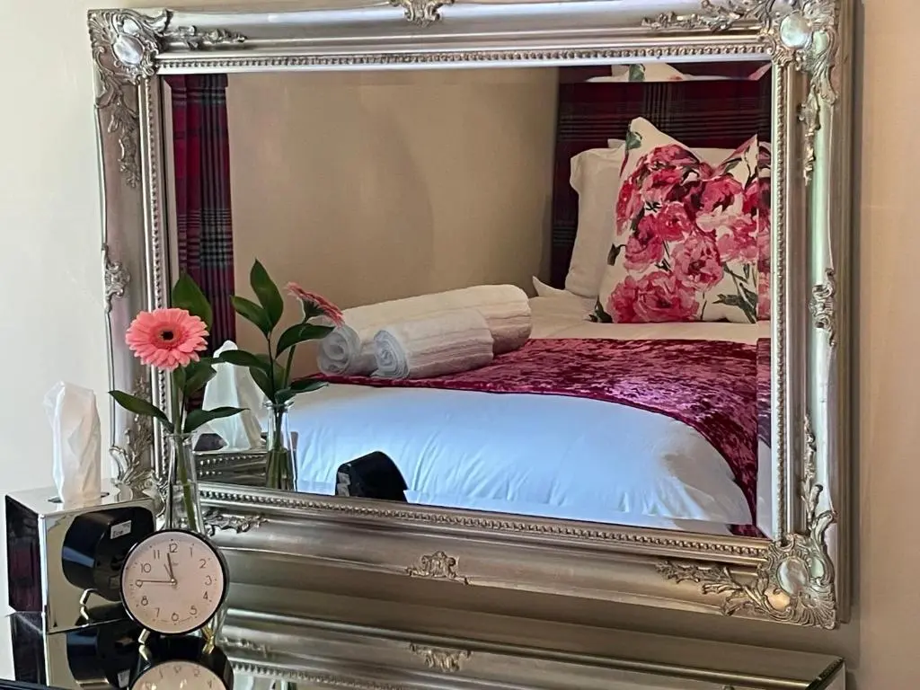 a mirror reflecting a bed in a room with flowers at Monkland Cottage in Nairn
