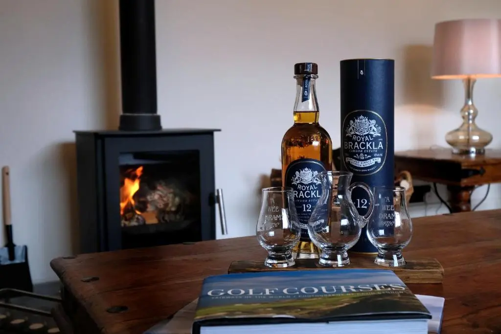 a bottle of wine and glasses on a table with a book at Monkland Cottage in Nairn