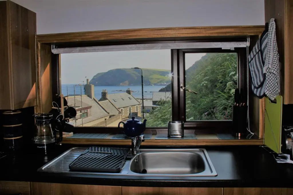 a kitchen sink with a window with a view of the ocean at Bellevue Holiday Cottage in Gardenstown