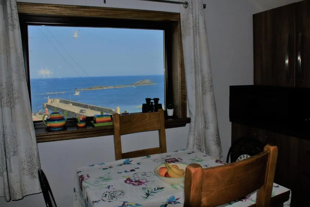 a table and a chair with a bowl of fruit in front of a window at Bellevue Holiday Cottage in Gardenstown