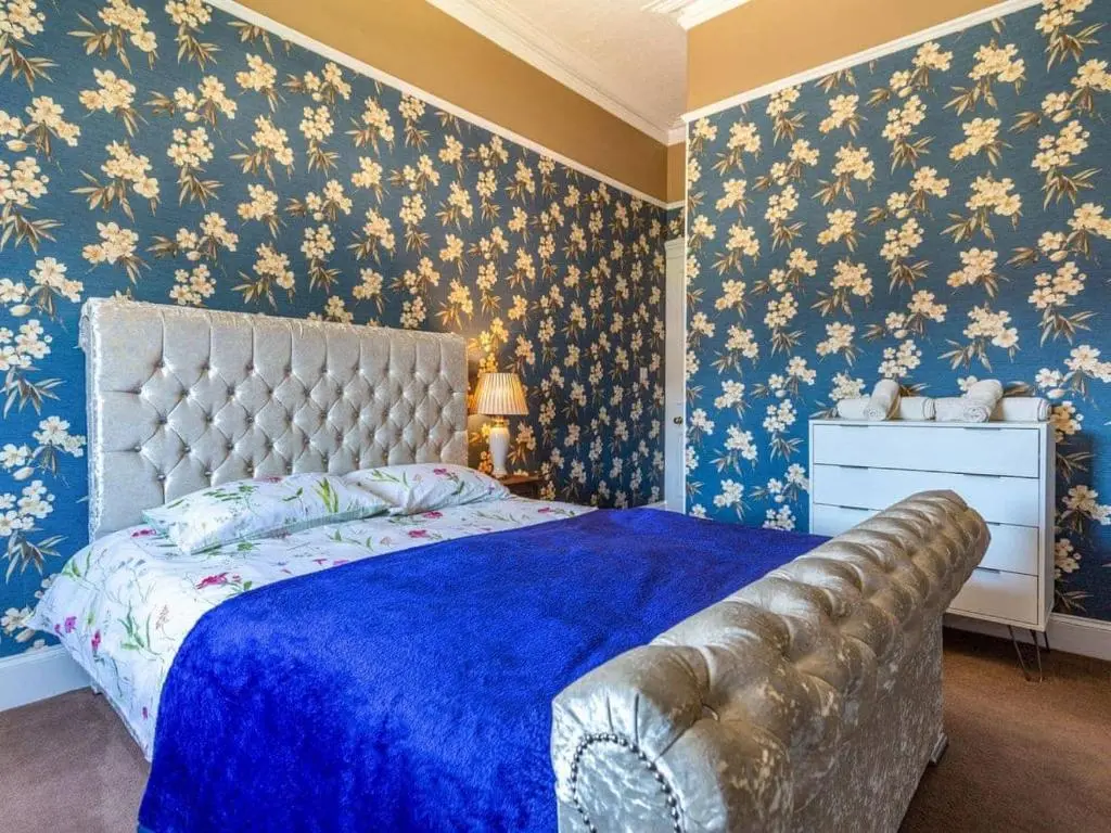 a bedroom with a blue bed with floral wallpaper at North Bank House in Lybster