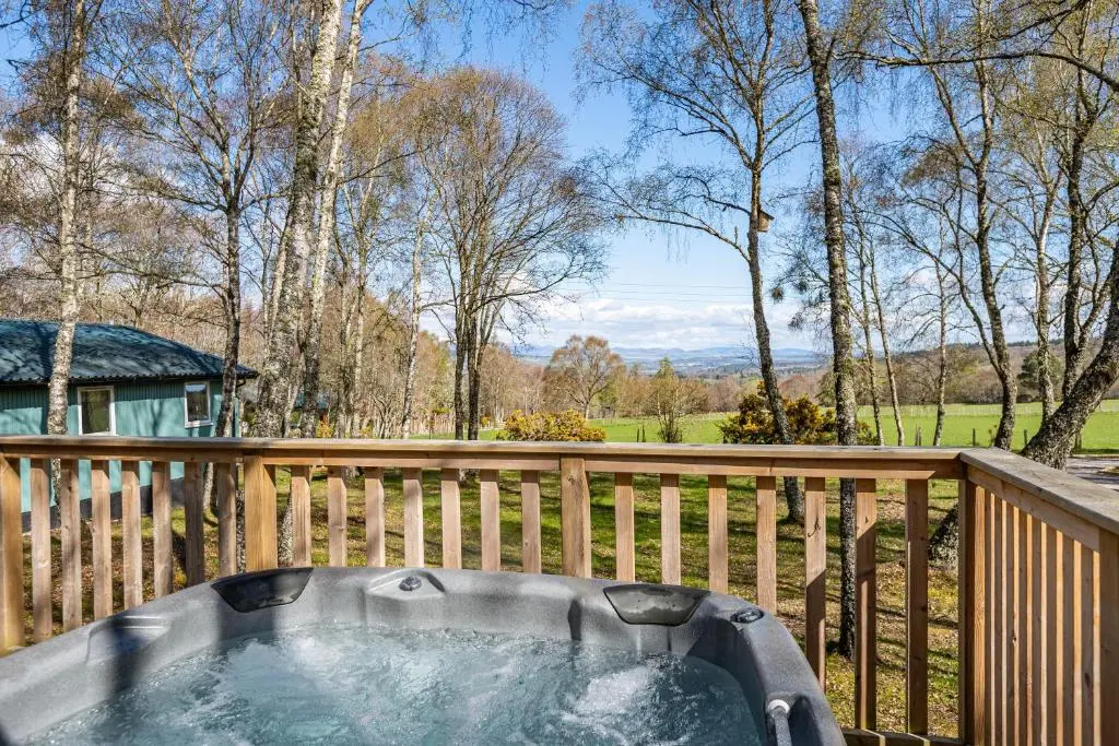 a hot tub on a deck with a wooden fence at Fern Lodge 2 with Hot Tub in Belladrum