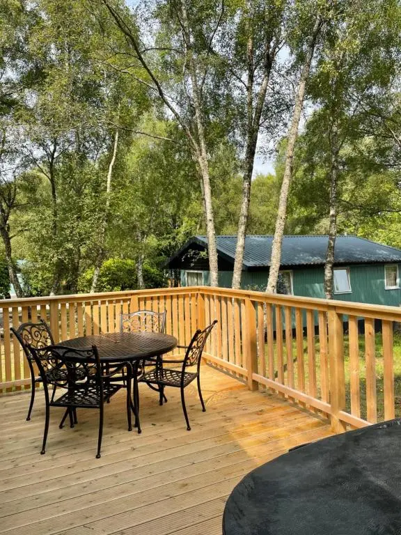 a patio with a table and chairs on a wooden deck at Fern Lodge 2 with Hot Tub in Belladrum