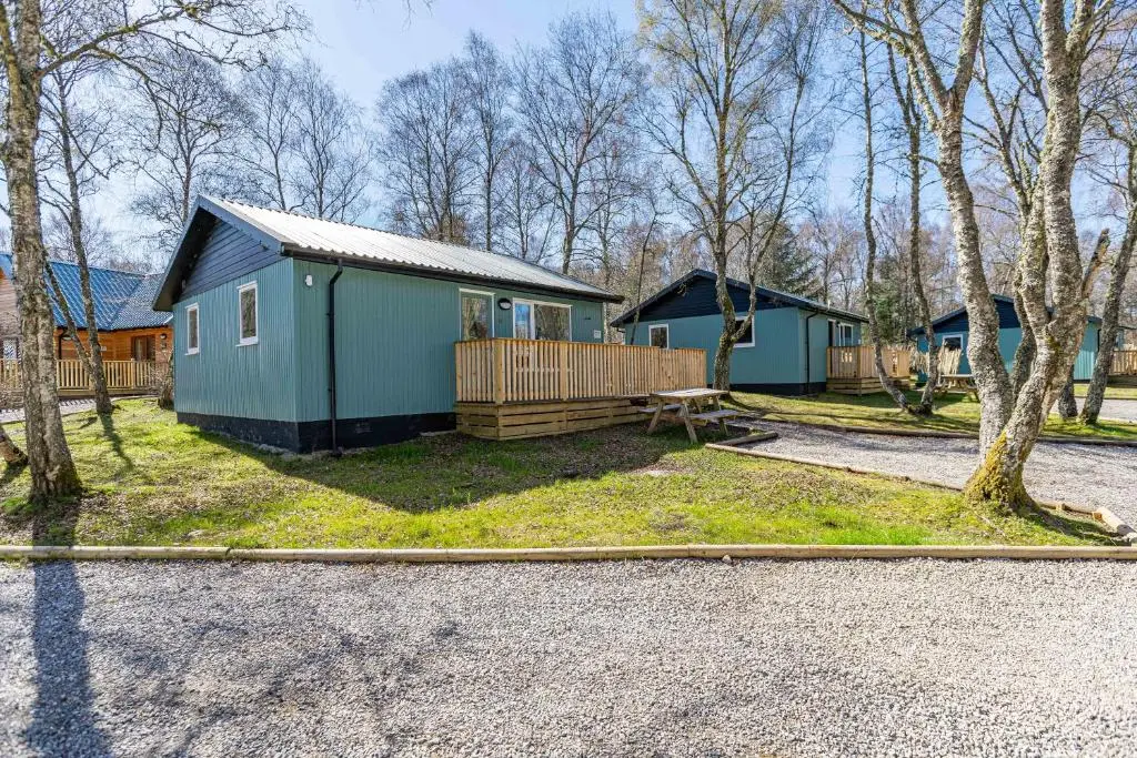 a small blue house with a fence and trees at Bracken Lodge 5 with Hot Tub in Belladrum