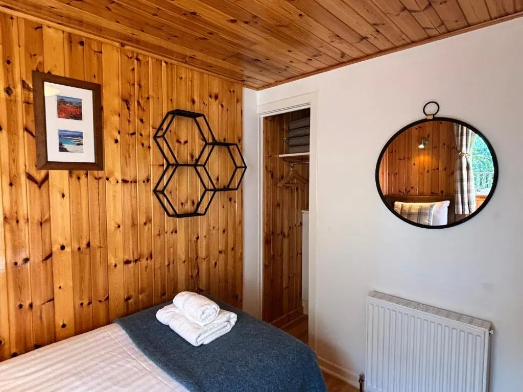 a bedroom with wooden walls and a bed with a mirror at Bracken Lodge 7 with Hot Tub in Belladrum