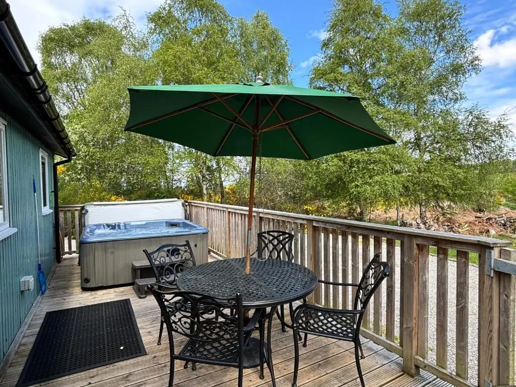 a table and chairs with an umbrella on a deck at Heather Lodge 17 with Hot Tub in Belladrum