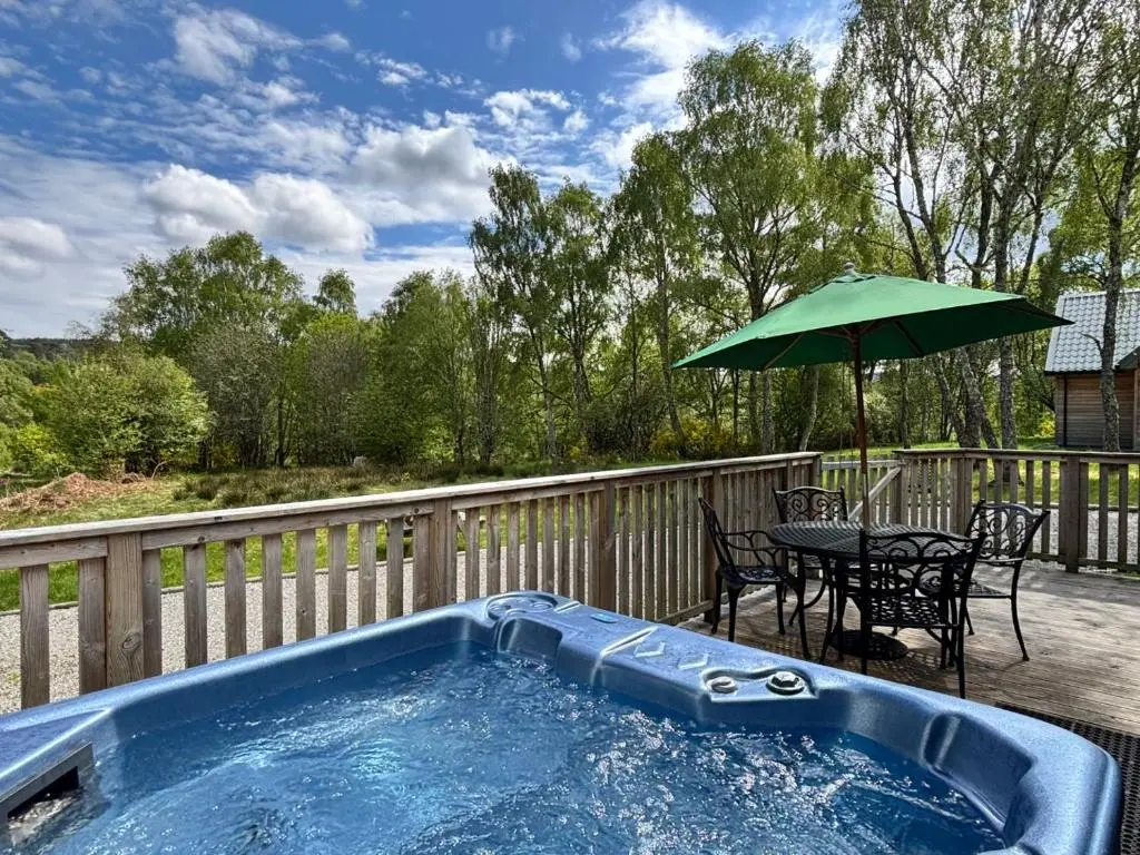 a hot tub on a deck with a table and an umbrella at Heather Lodge 17 with Hot Tub in Belladrum