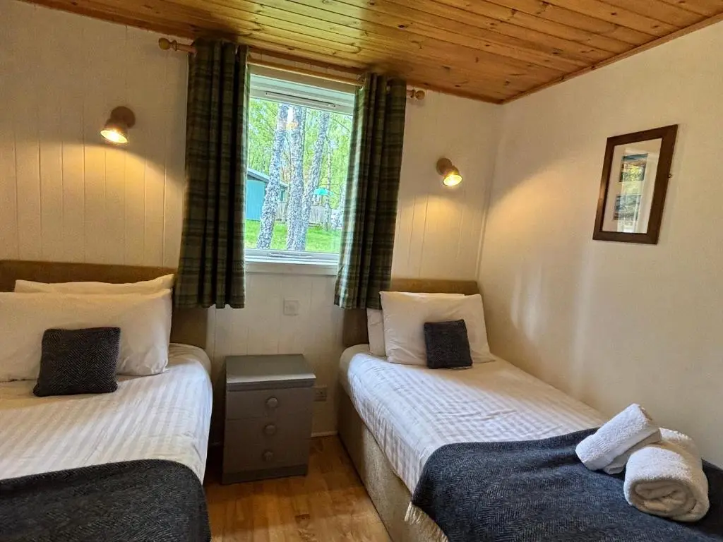two twin beds in a room with a window at Heather Lodge 17 with Hot Tub in Belladrum