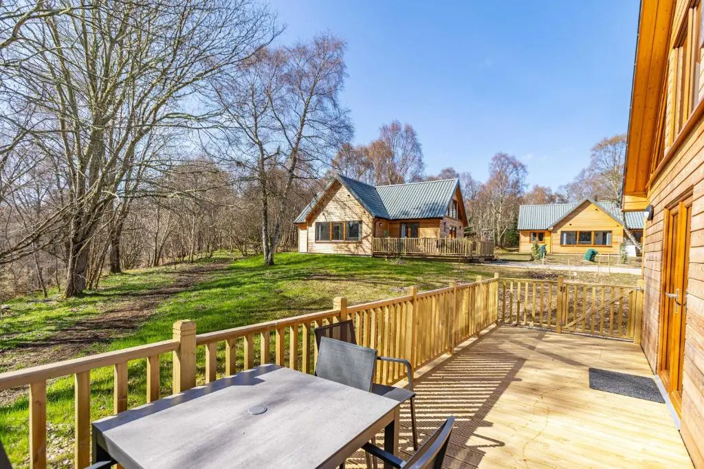 a wooden deck with a table and a house at Thistle Lodge 19 with Hot Tub in Belladrum