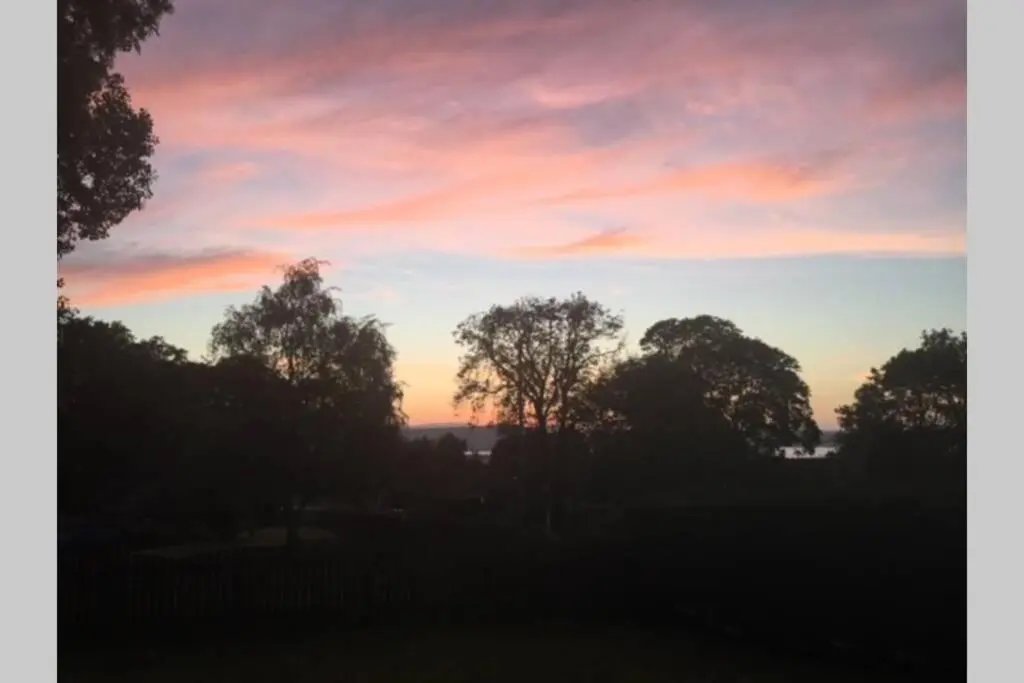 a sunset in a field with trees in the foreground at TomaX Garden Cabin Free Parking in Inverness
