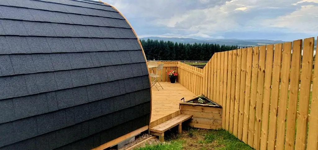 a backyard with a wooden fence and a wooden bench at The Pod at Hollingwell House - Glamping NC500 Edderton in Balblair