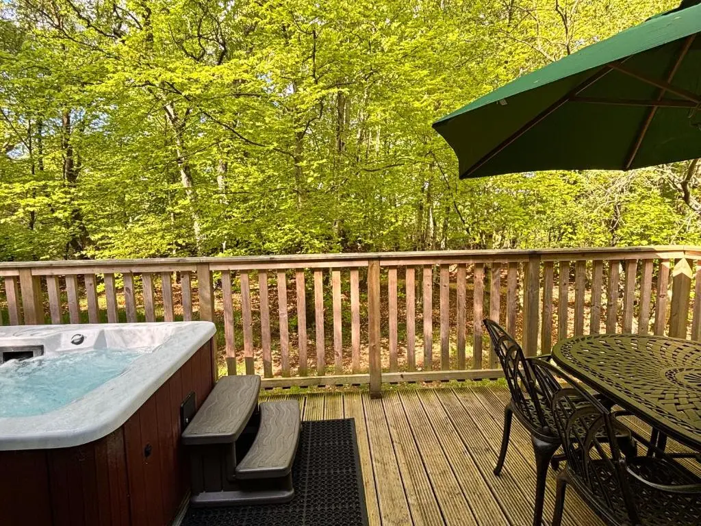 a hot tub on a deck with a table and an umbrella at Fern Lodge 11 with Hot Tub in Belladrum