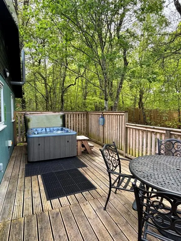 a deck with a hot tub and a table and chairs at Bracken Lodge 8 with Hot Tub in Belladrum