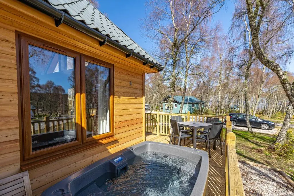 a hot tub on a deck next to a house at Thistle Lodge 20 with Hot Tub in Belladrum