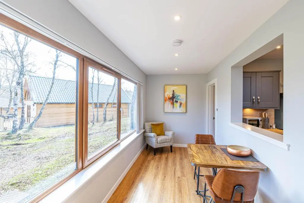 a kitchen and dining room with a table and windows at Thistle Lodge 22 with Hot Tub in Belladrum
