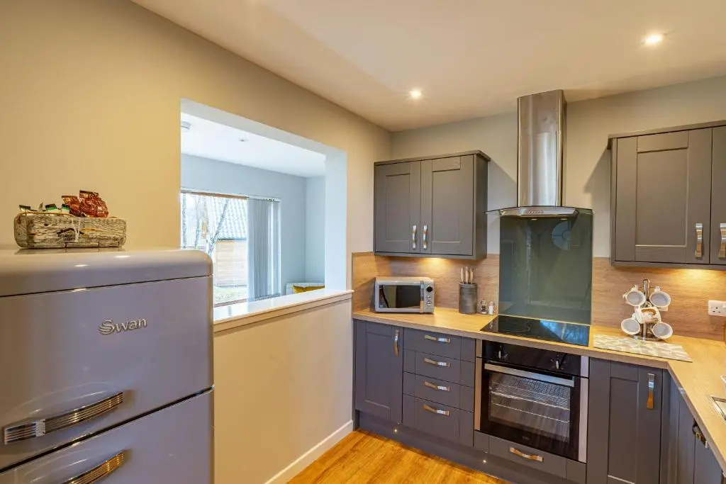 a kitchen with gray cabinets and a stove at Thistle Lodge 22 with Hot Tub in Belladrum