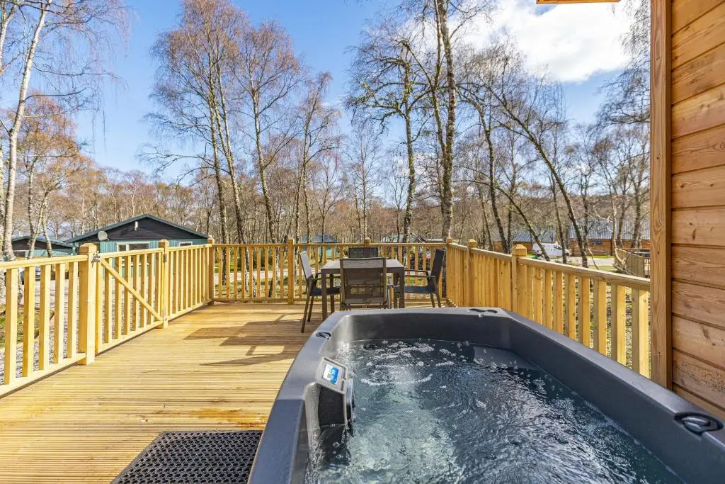 a hot tub on a deck with a table at Thistle Lodge 22 with Hot Tub in Belladrum