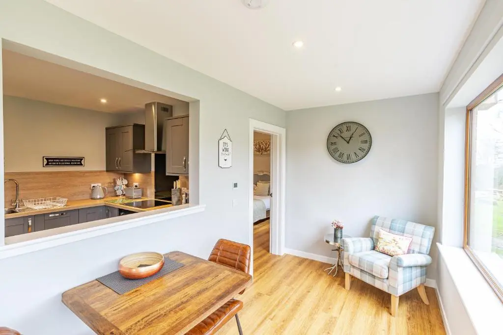 a kitchen with a table and a clock on the wall at Thistle Lodge 18 with Hot Tub in Belladrum