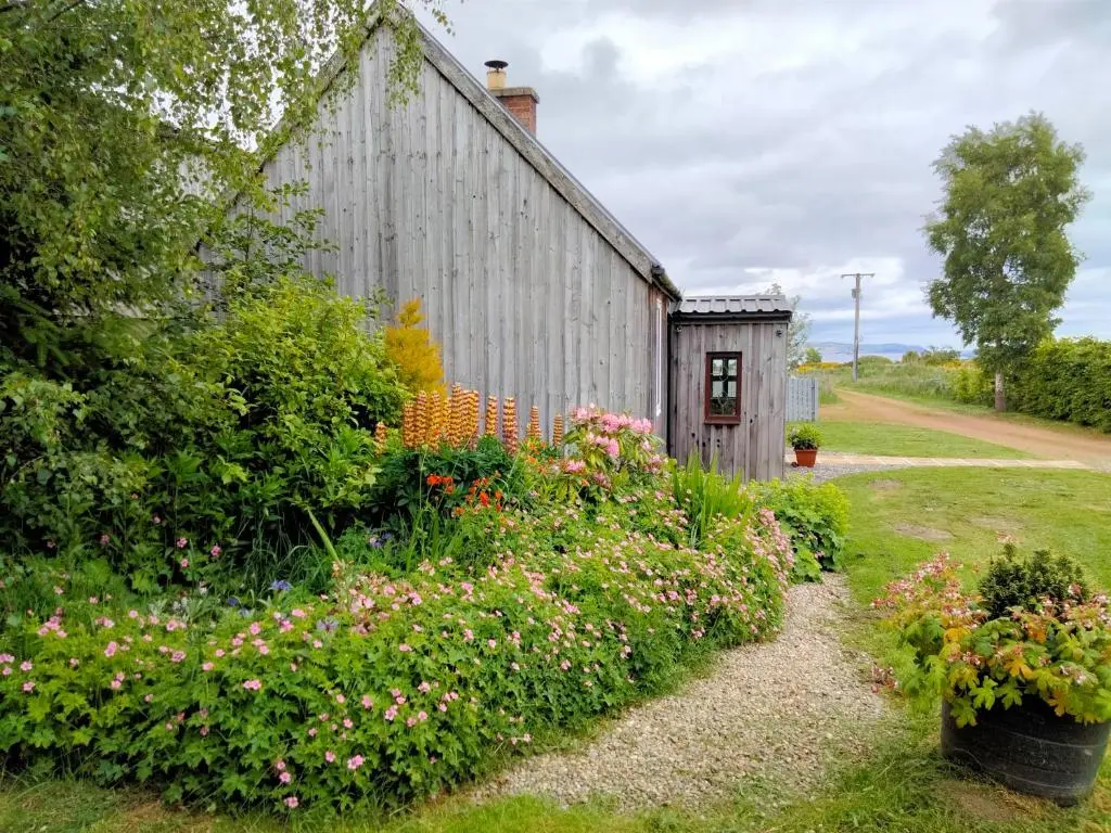 a garden with flowers next to a barn at Small cosy bothy in Dingwall