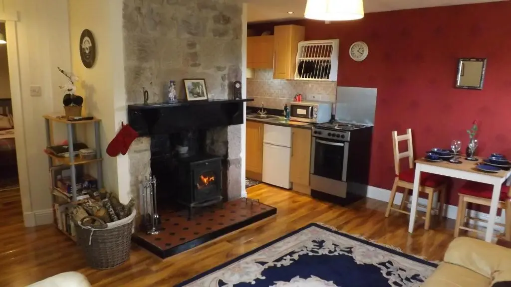 a living room with a fireplace and a kitchen at Small cosy bothy in Dingwall